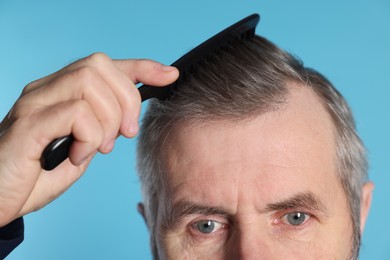 Photo of Man combing his hair on light blue background, closeup