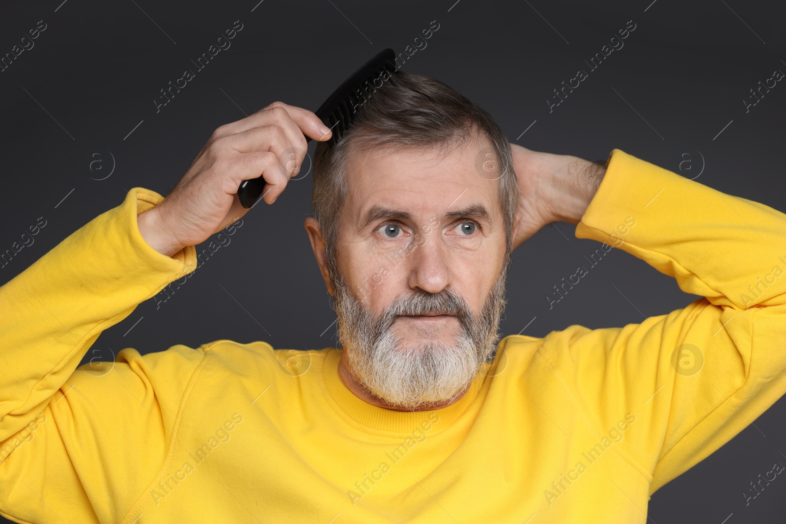 Photo of Handsome man combing his hair on dark grey background