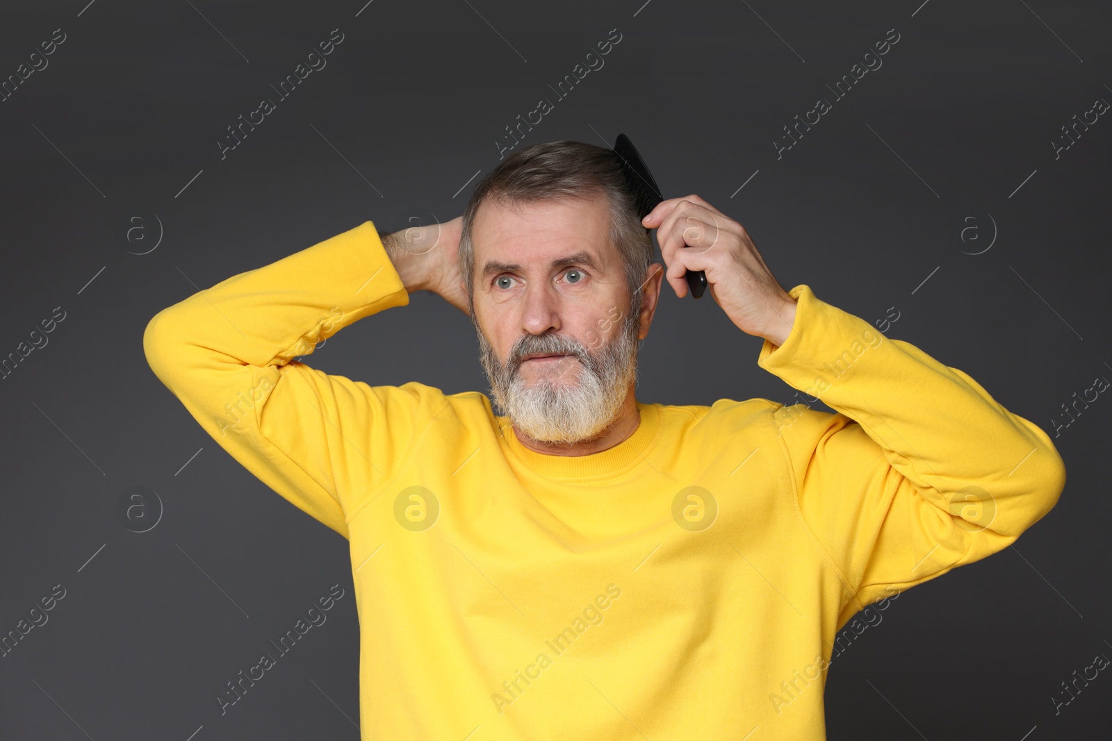 Photo of Handsome man combing his hair on dark grey background