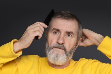 Photo of Handsome man combing his hair on dark grey background