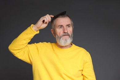 Photo of Handsome man combing his hair on dark grey background