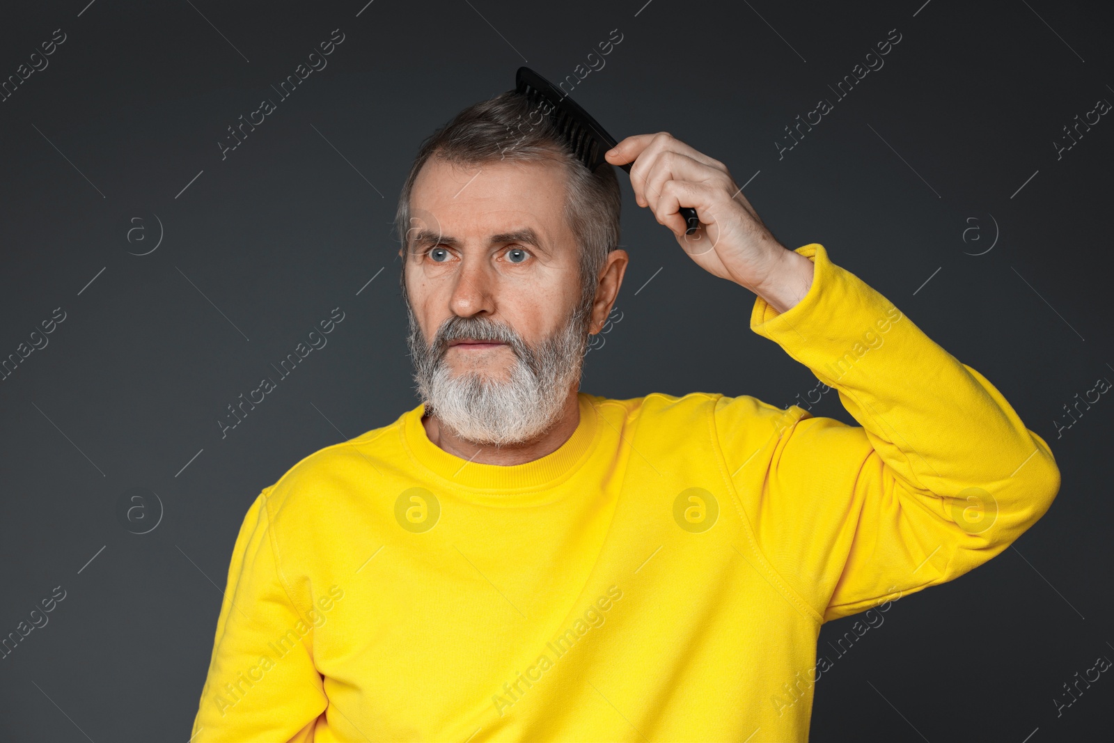 Photo of Handsome man combing his hair on dark grey background