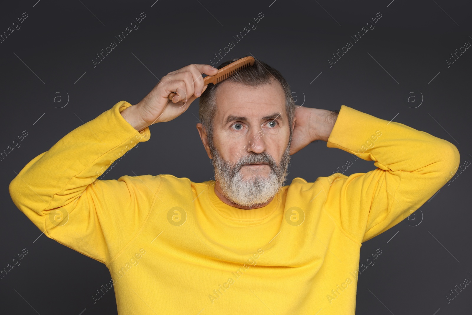 Photo of Handsome man combing his hair on dark grey background