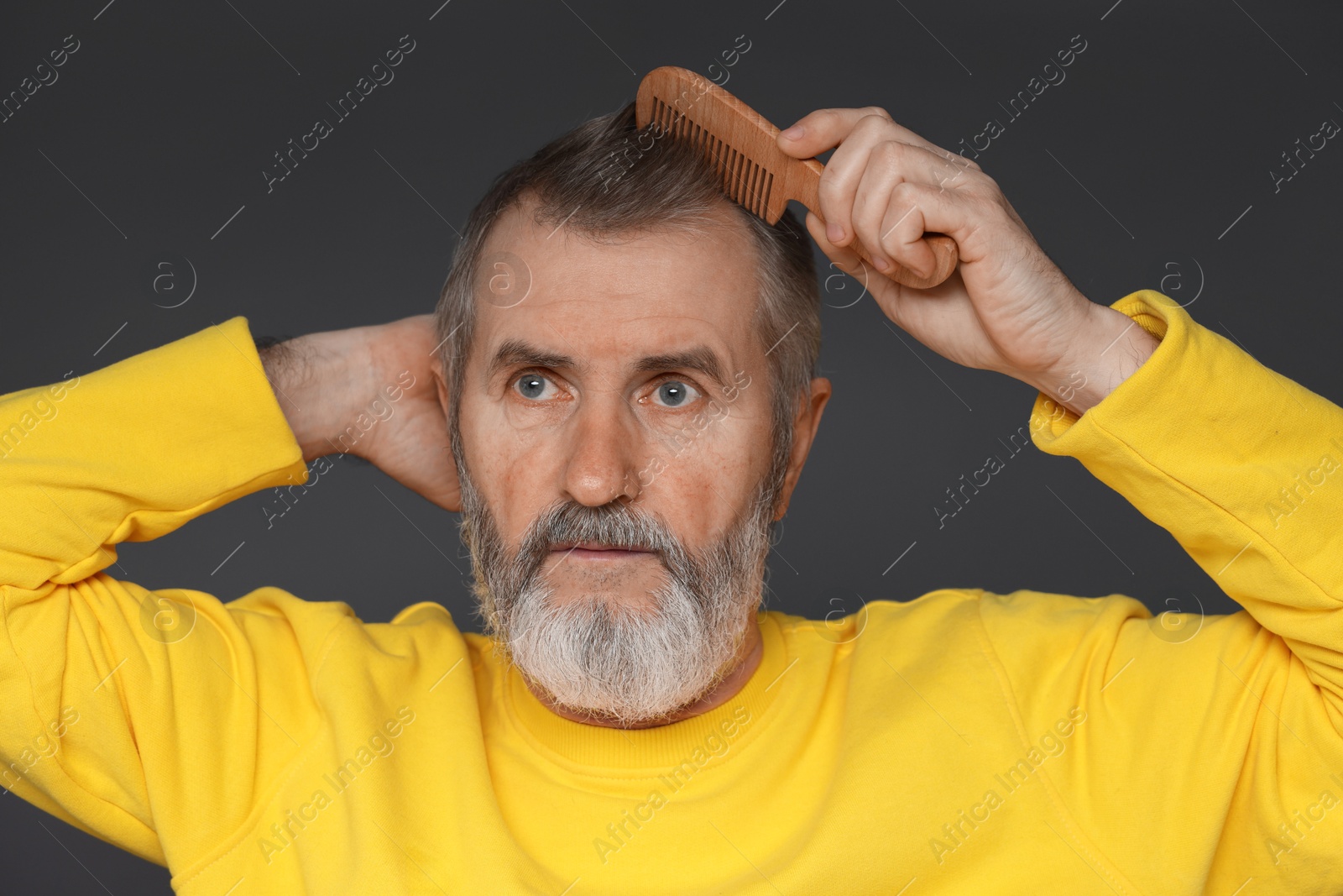 Photo of Handsome man combing his hair on dark grey background