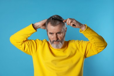 Photo of Handsome man combing his hair on light blue background