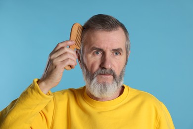 Photo of Handsome man combing his hair on light blue background