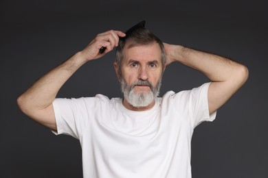 Photo of Handsome man combing his hair on dark grey background