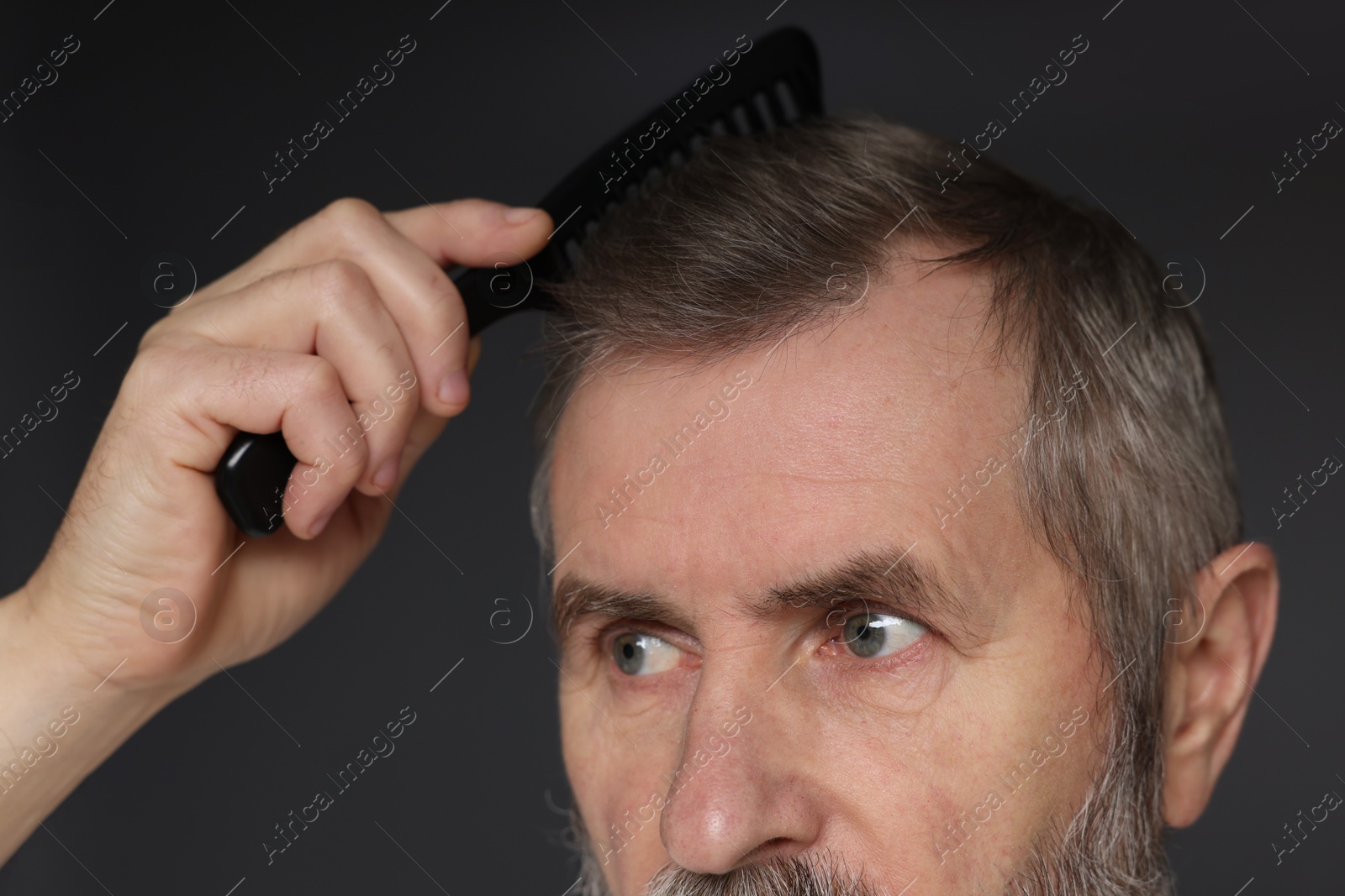 Photo of Man combing his hair on dark grey background, closeup