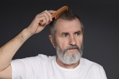 Photo of Handsome man combing his hair on dark grey background