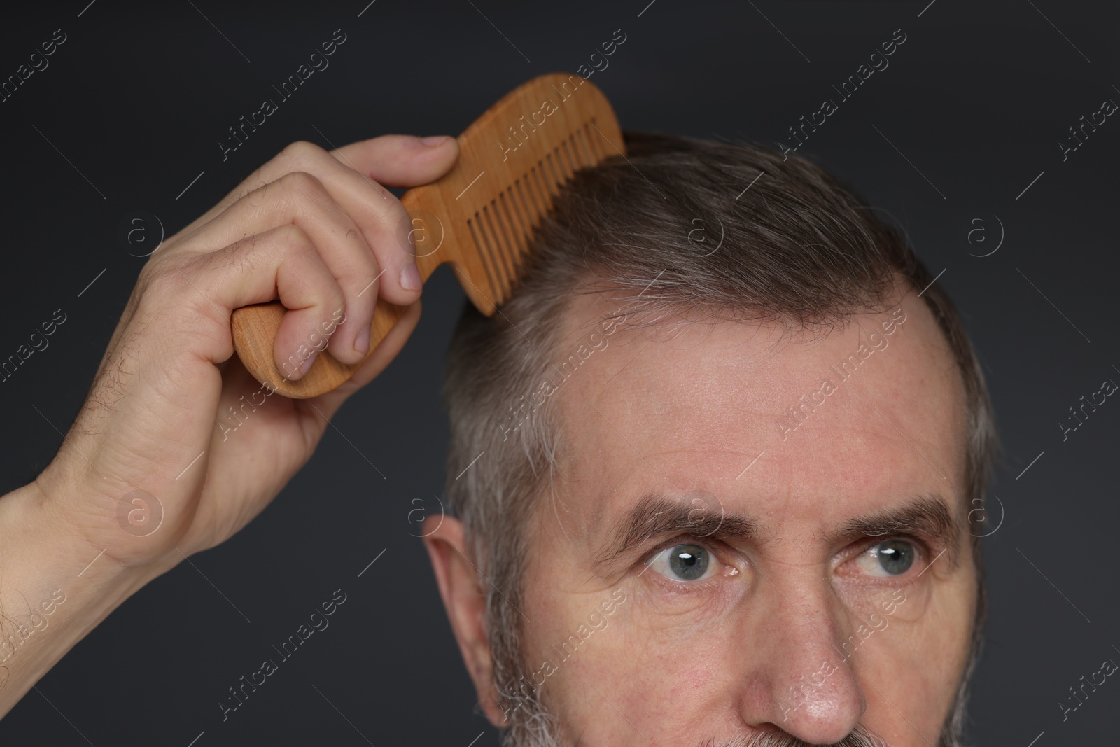 Photo of Man combing his hair on dark grey background, closeup