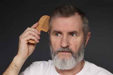 Photo of Handsome man combing his hair on dark grey background, closeup