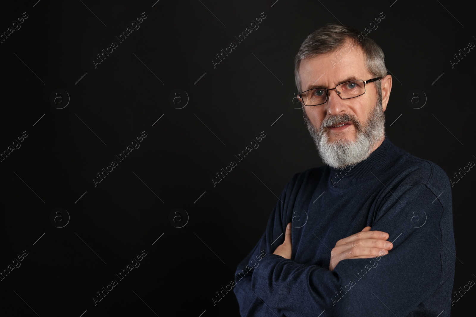 Photo of Portrait of mature man with crossed arms on black background, space for text