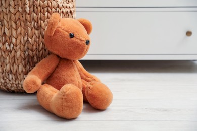 Photo of Teddy bear near basket on floor at home, space for text