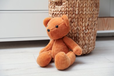 Photo of Teddy bear near basket on floor at home