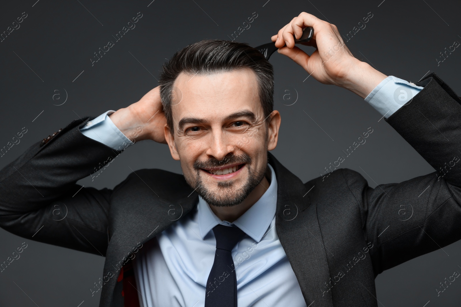 Photo of Handsome businessman combing his hair on dark background