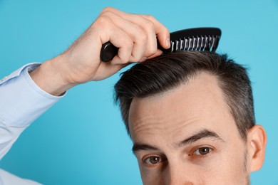 Photo of Handsome man stylish his hair with comb on light blue background, closeup