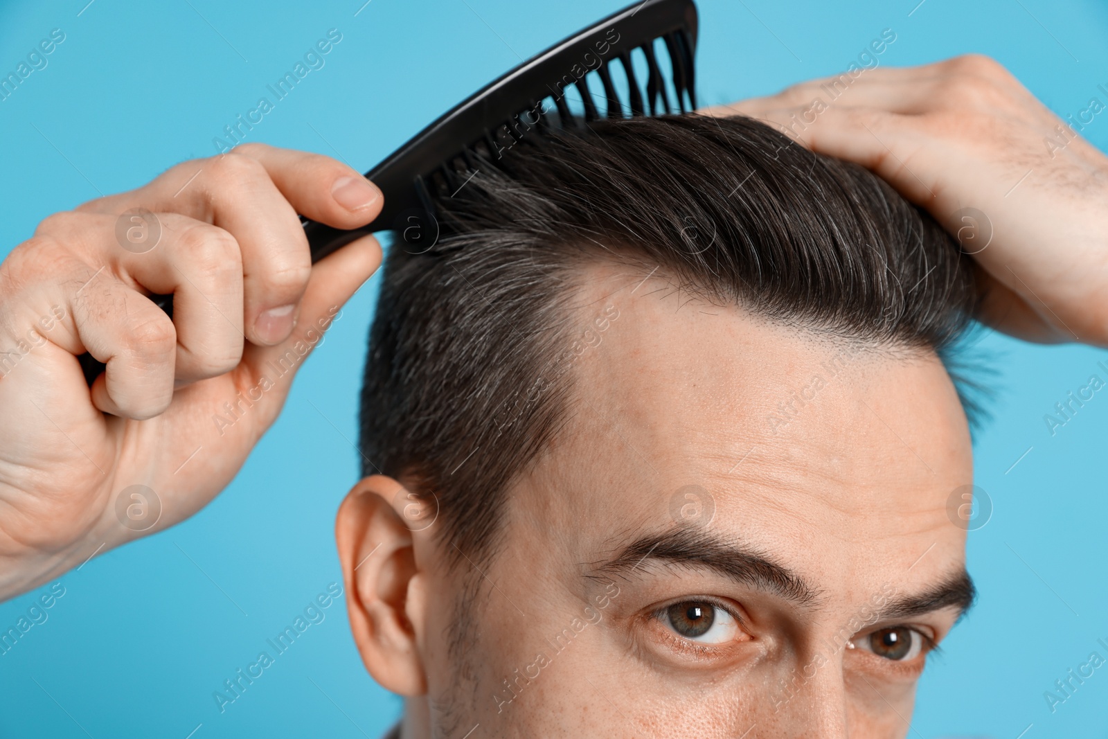 Photo of Handsome man stylish his hair with comb on light blue background, closeup