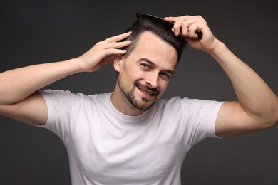 Photo of Handsome man combing his hair on dark background