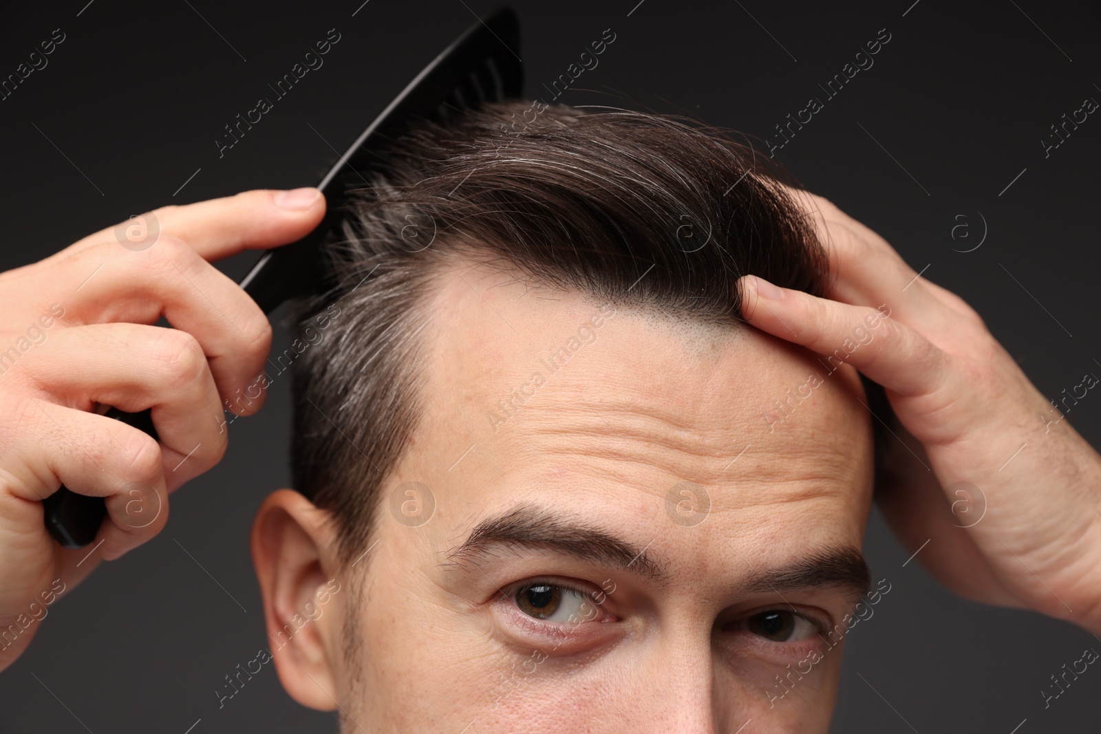 Photo of Handsome man combing his hair on dark background, closeup