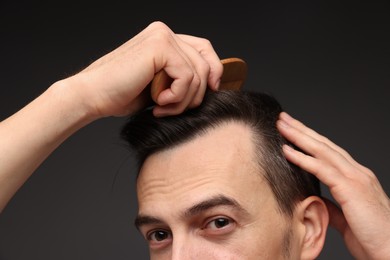 Photo of Handsome man combing his hair on dark background, closeup