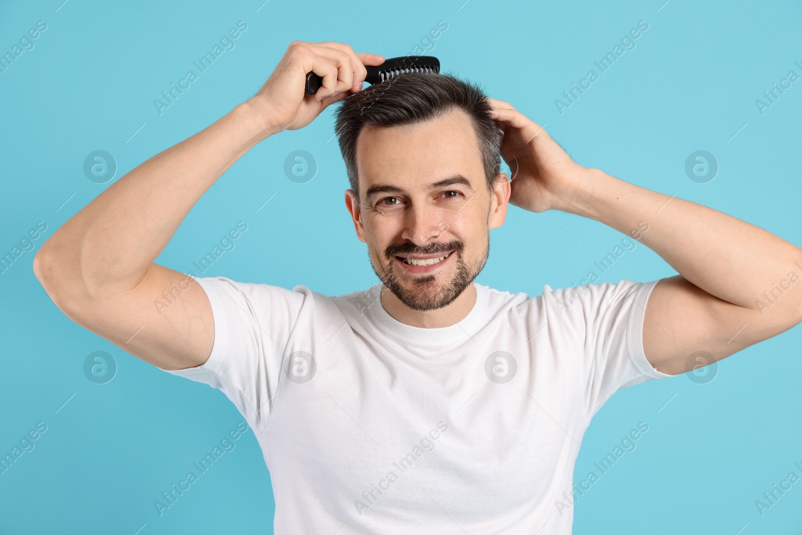 Photo of Handsome man stylish his hair with comb on light blue background