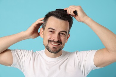 Photo of Handsome man stylish his hair with comb on light blue background