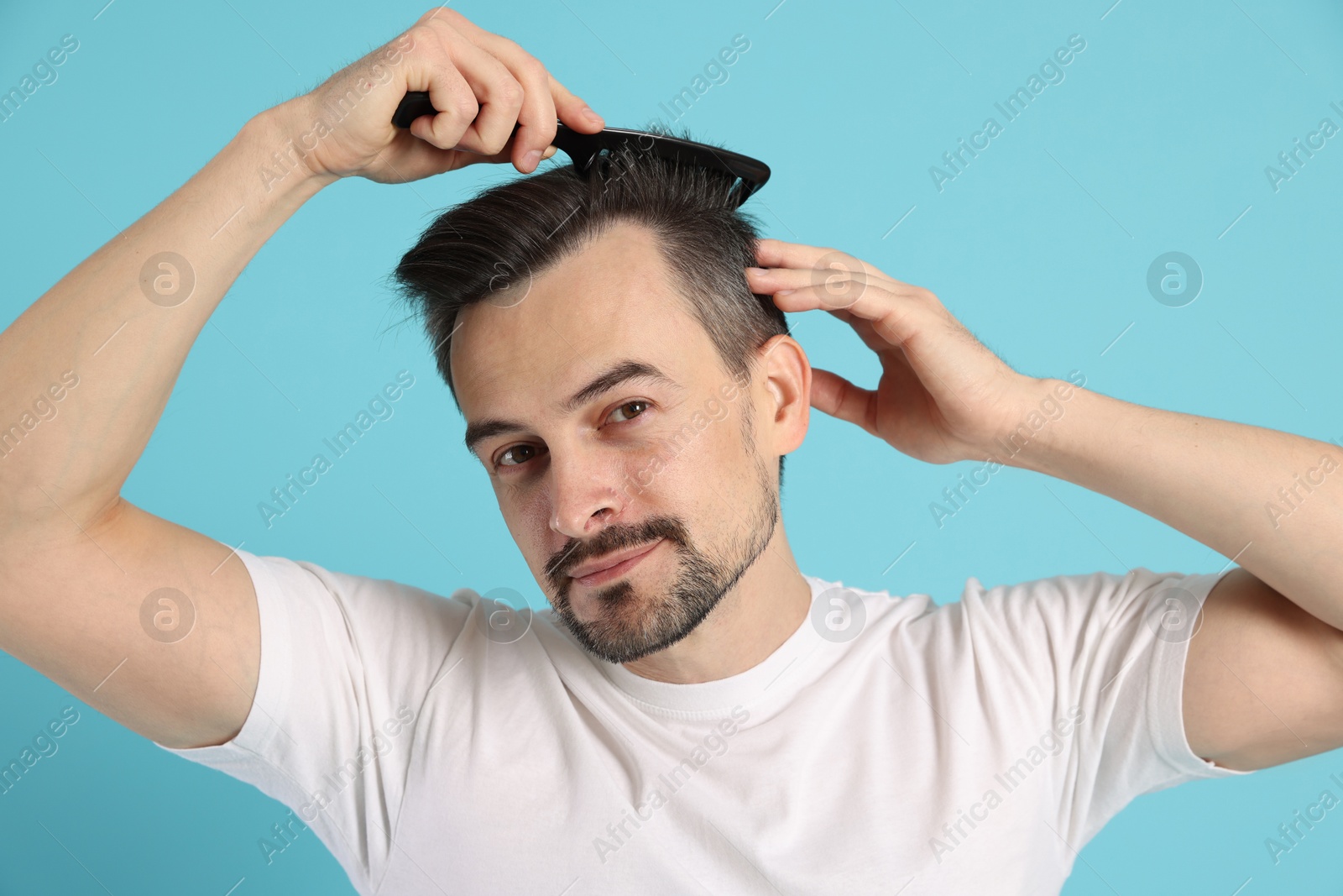 Photo of Handsome man stylish his hair with comb on light blue background