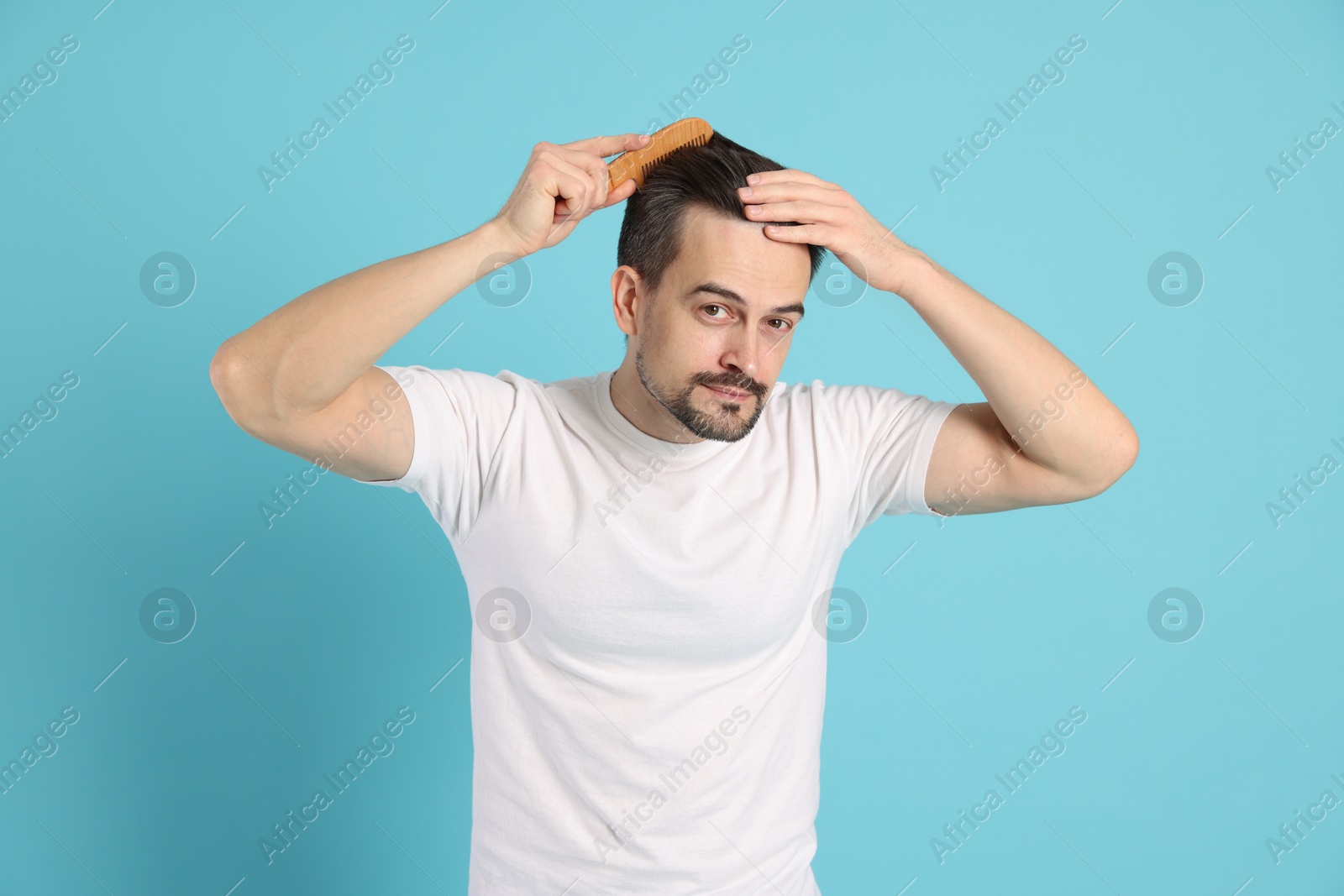 Photo of Handsome man stylish his hair with comb on light blue background