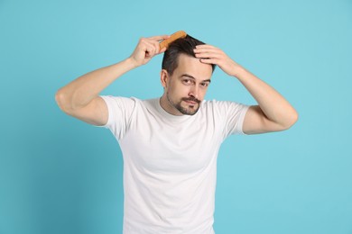 Photo of Handsome man stylish his hair with comb on light blue background