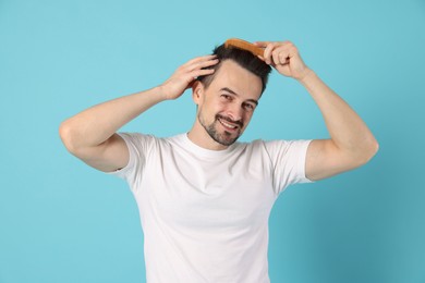 Photo of Handsome man stylish his hair with comb on light blue background