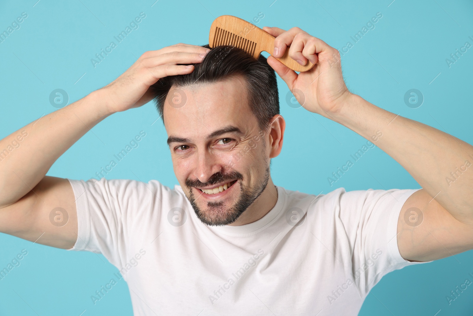 Photo of Handsome man stylish his hair with comb on light blue background