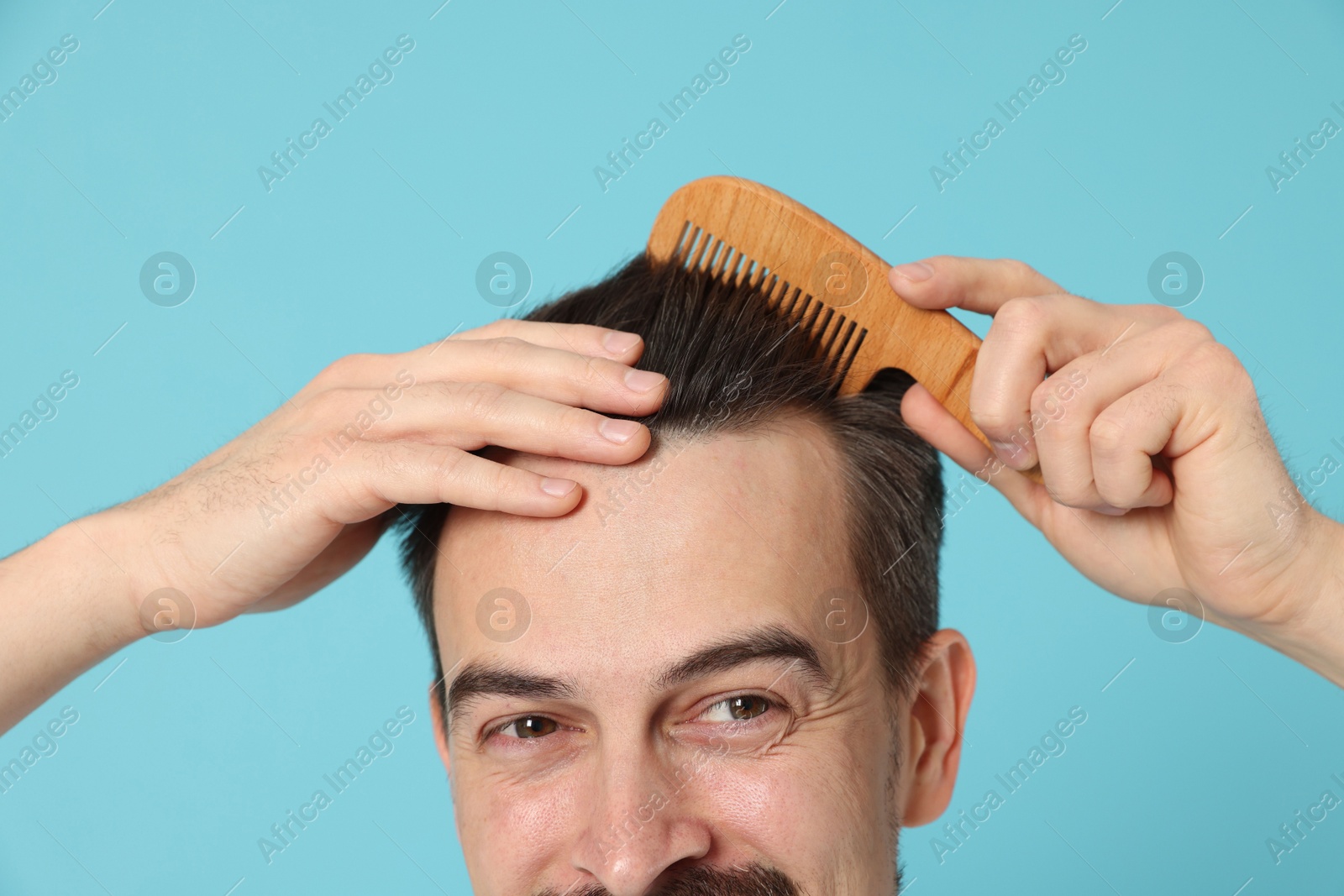 Photo of Handsome man stylish his hair with comb on light blue background, closeup