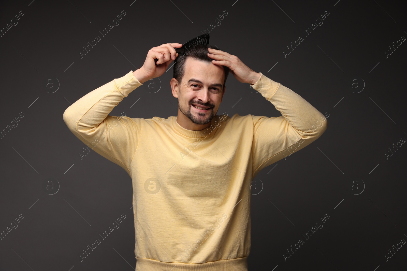 Photo of Handsome man combing his hair on dark background