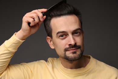 Photo of Handsome man combing his hair on dark background