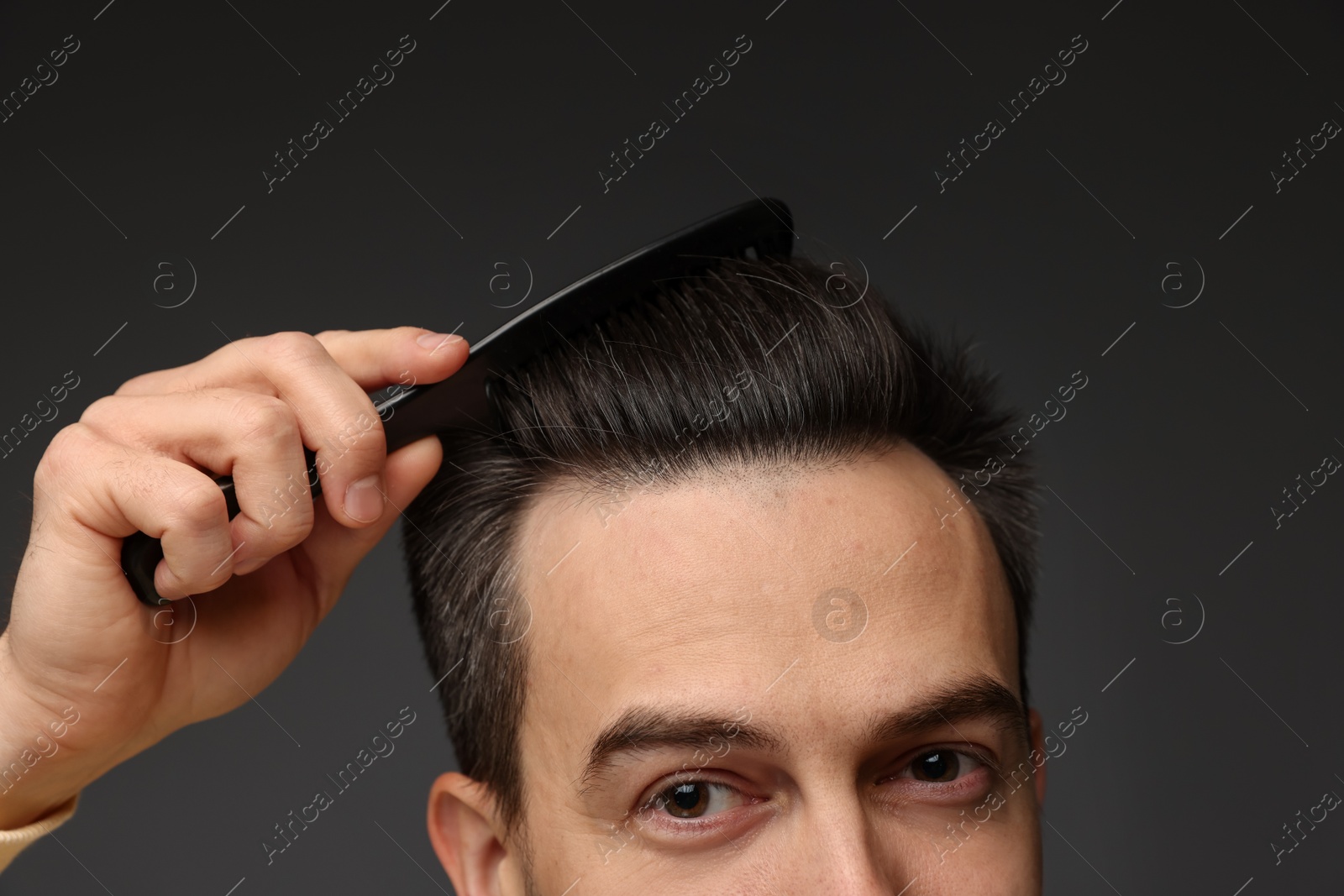 Photo of Handsome man combing his hair on dark background, closeup