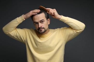 Photo of Handsome man combing his hair on dark background