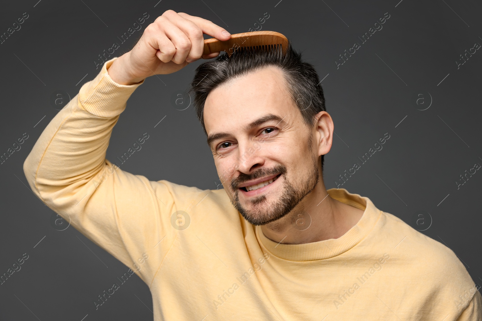 Photo of Handsome man combing his hair on dark background