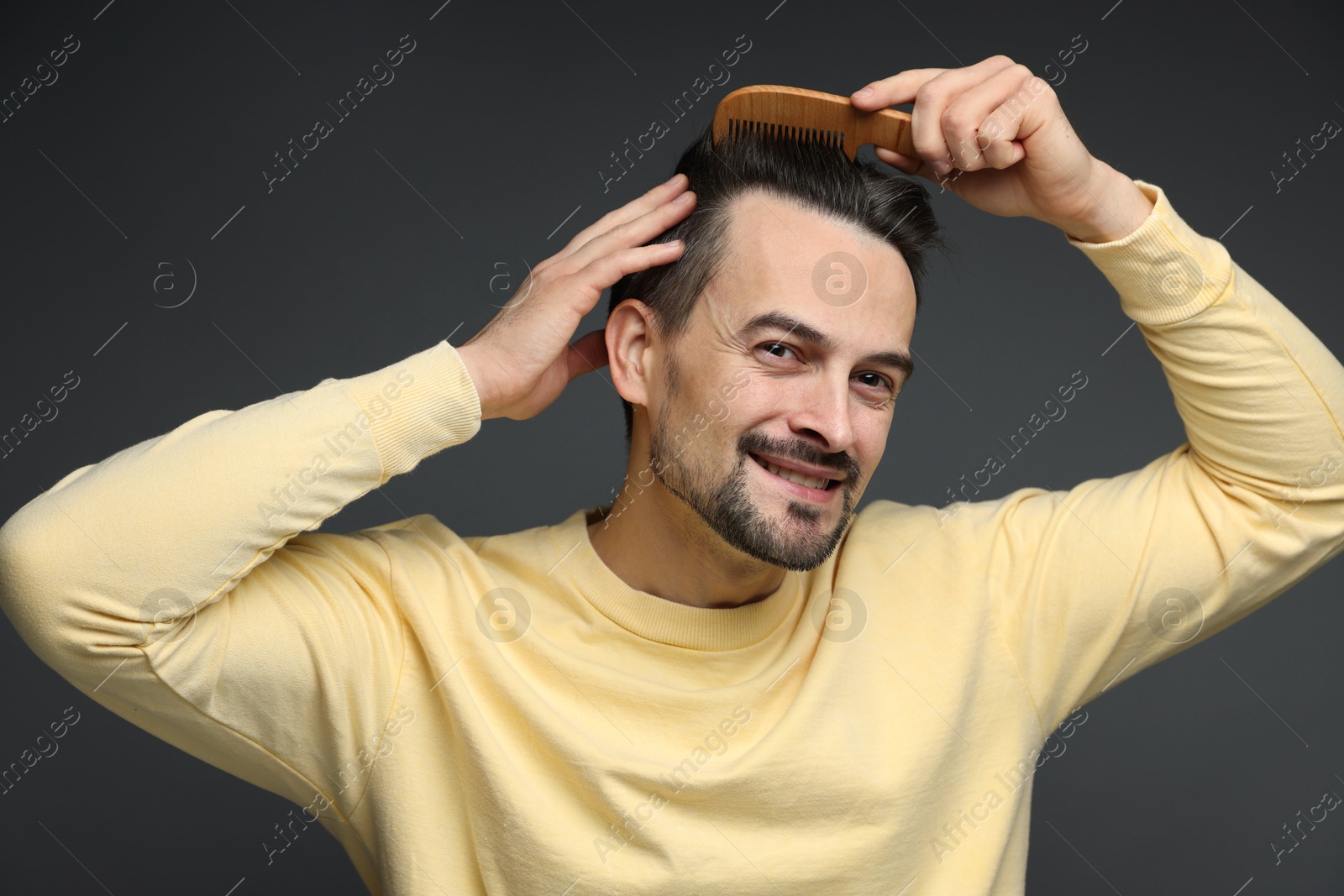 Photo of Handsome man combing his hair on dark background