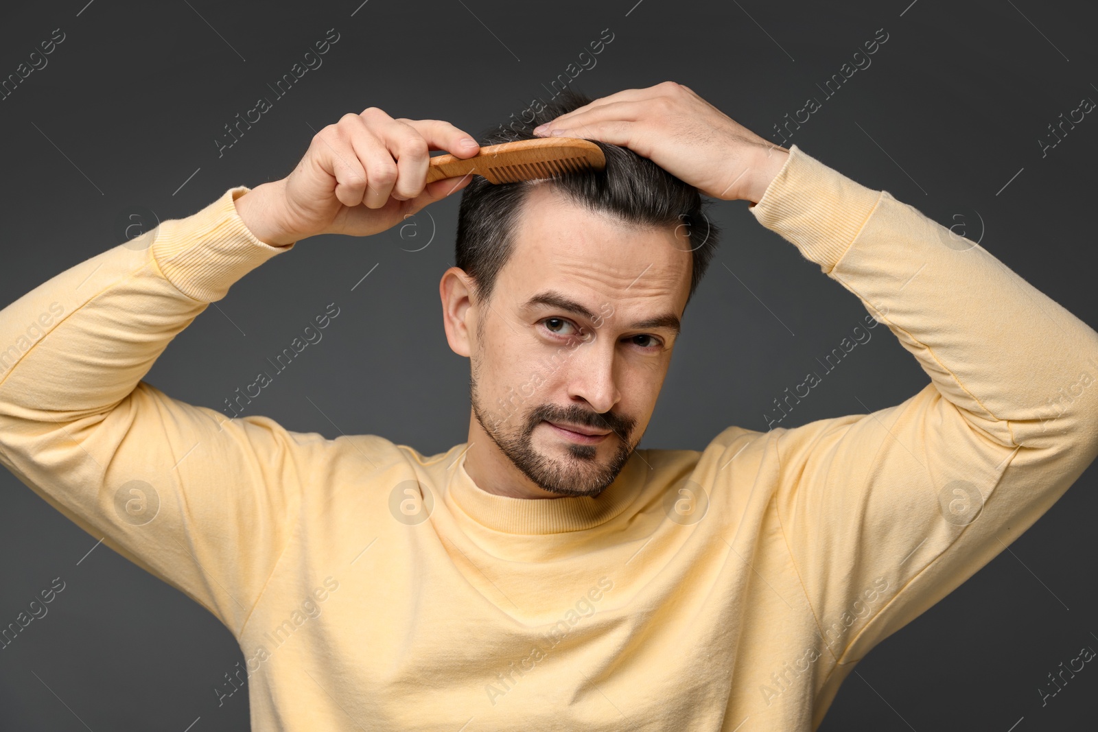 Photo of Handsome man combing his hair on dark background