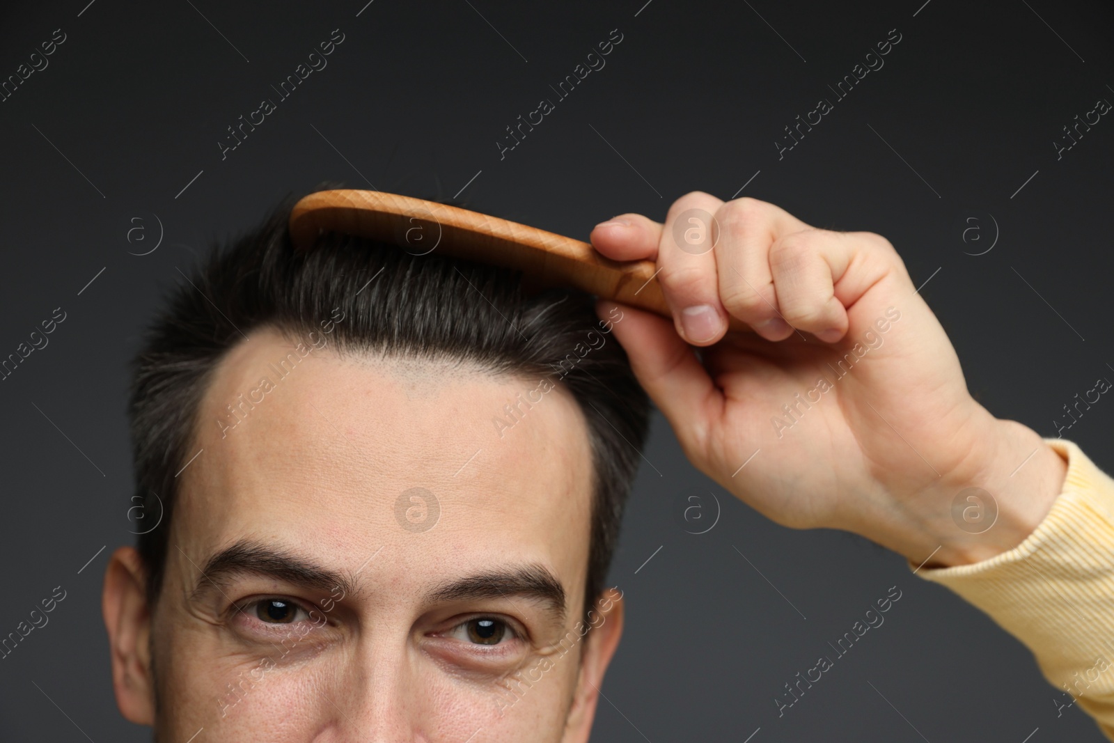 Photo of Handsome man combing his hair on dark background, closeup