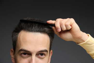 Photo of Handsome man combing his hair on dark background, closeup