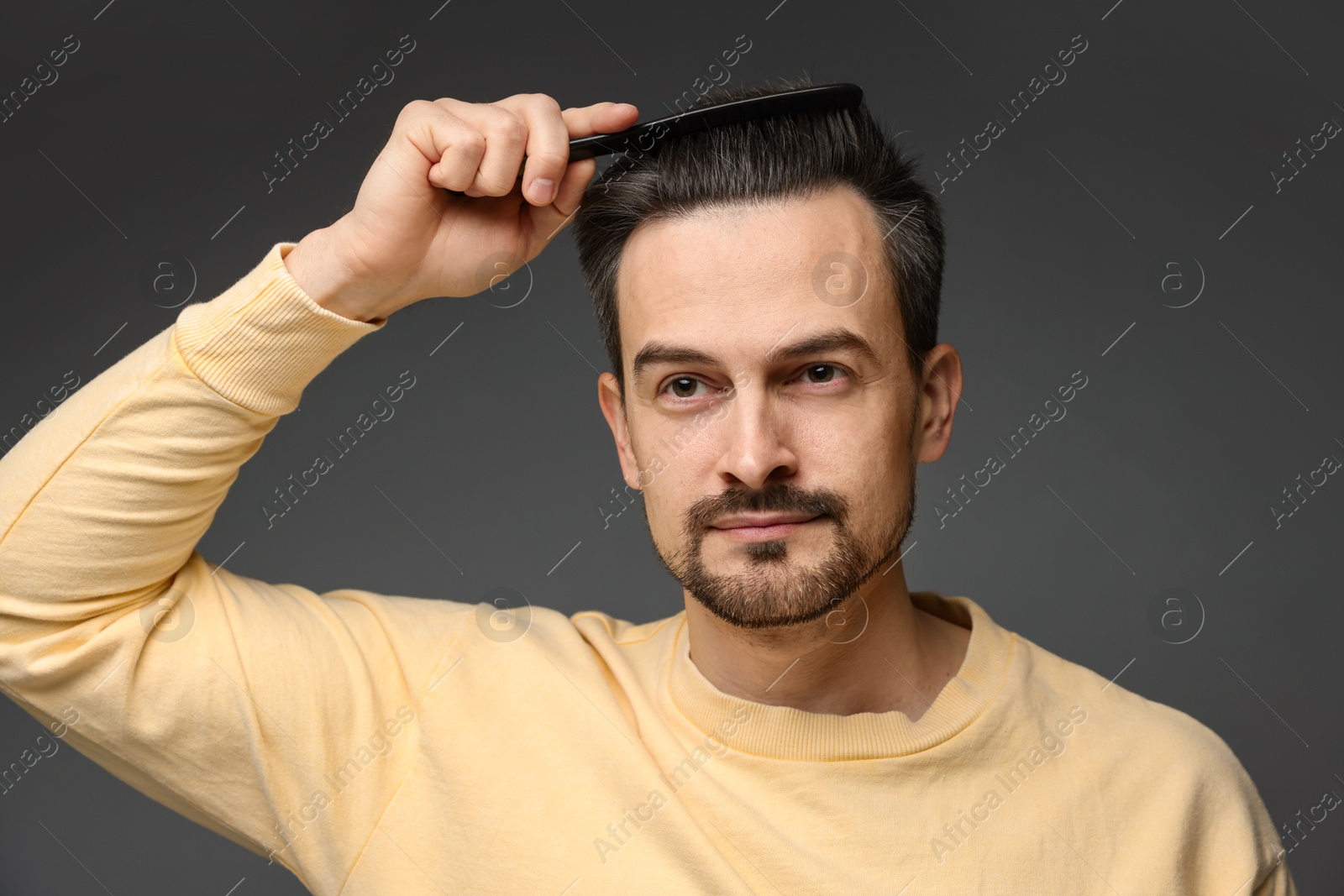 Photo of Handsome man combing his hair on dark background