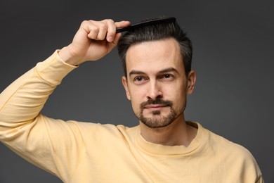 Photo of Handsome man combing his hair on dark background