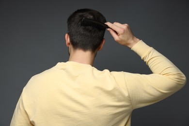 Photo of Man combing his hair on dark background, back view