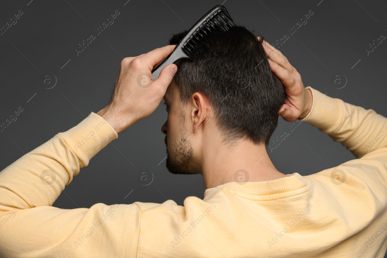 Photo of Man combing his hair on dark background, back view