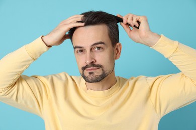 Photo of Handsome man stylish his hair with comb on light blue background