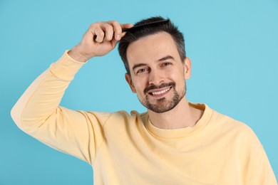 Photo of Handsome man stylish his hair with comb on light blue background