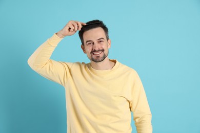 Photo of Handsome man stylish his hair with comb on light blue background