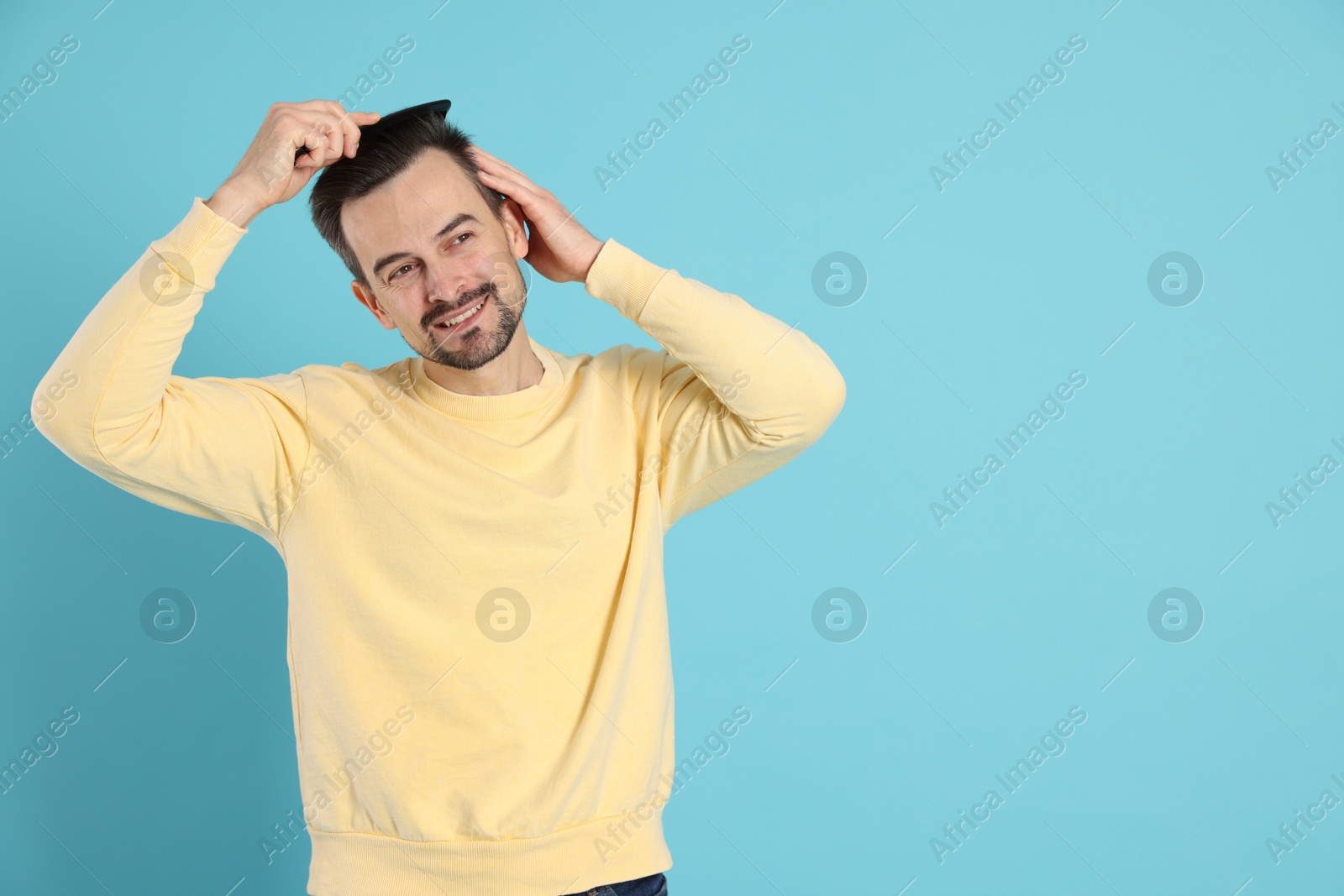 Photo of Handsome man stylish his hair with comb on light blue background