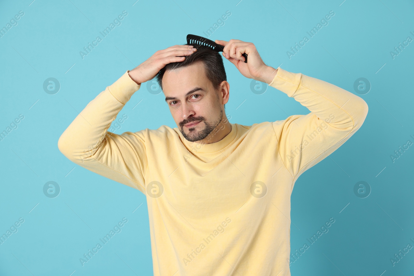 Photo of Handsome man stylish his hair with comb on light blue background